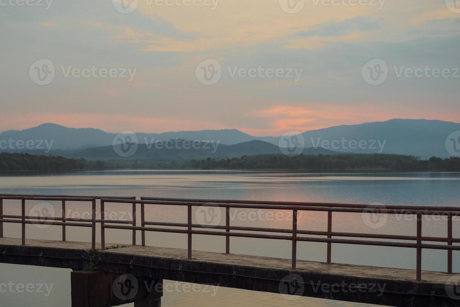 The concrete walkway into the water reservoir with the horizontal line of the mountains during the sunset photo