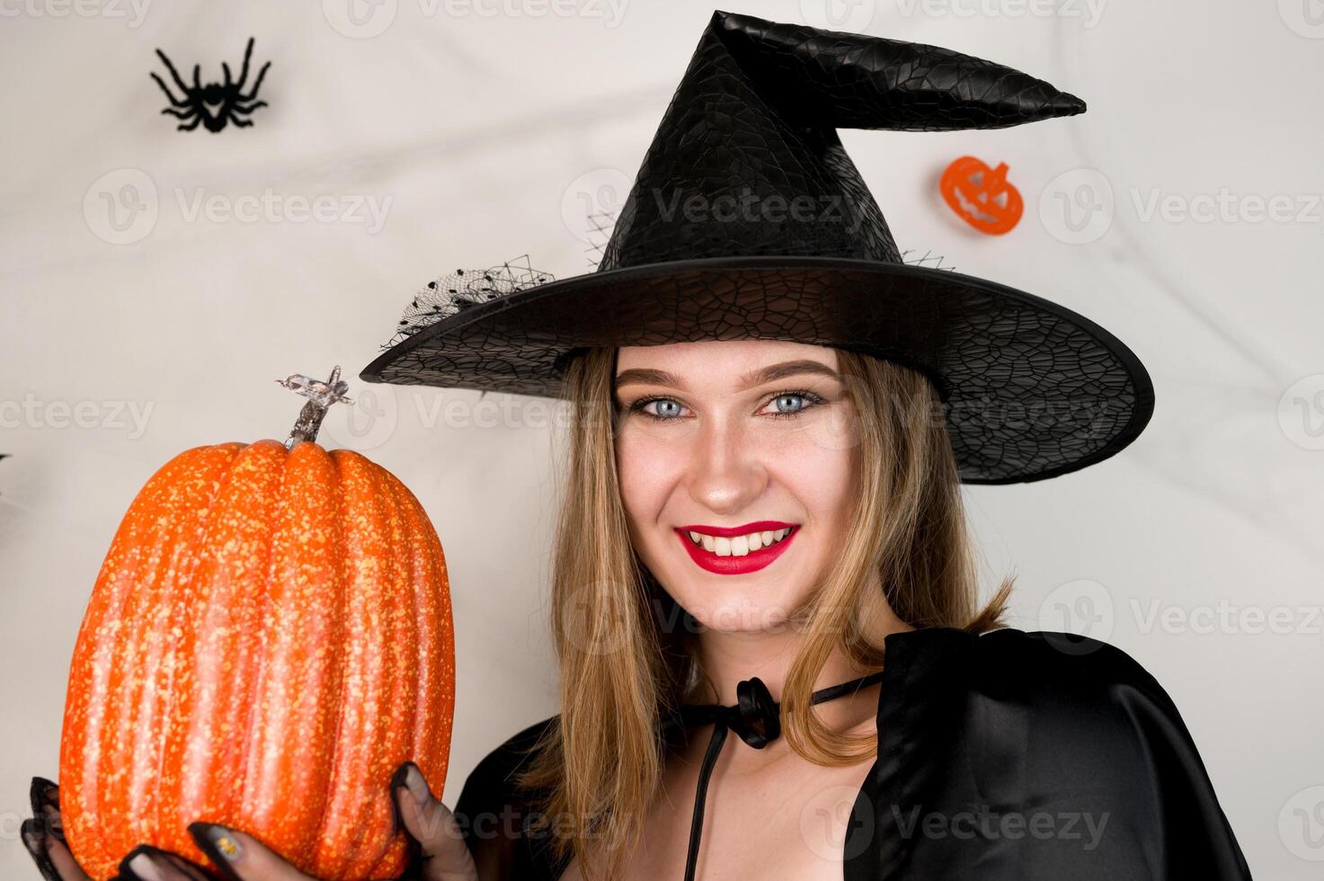 Beautiful woman in witch costume with pumpkin in hands against background with spiderweb. photo