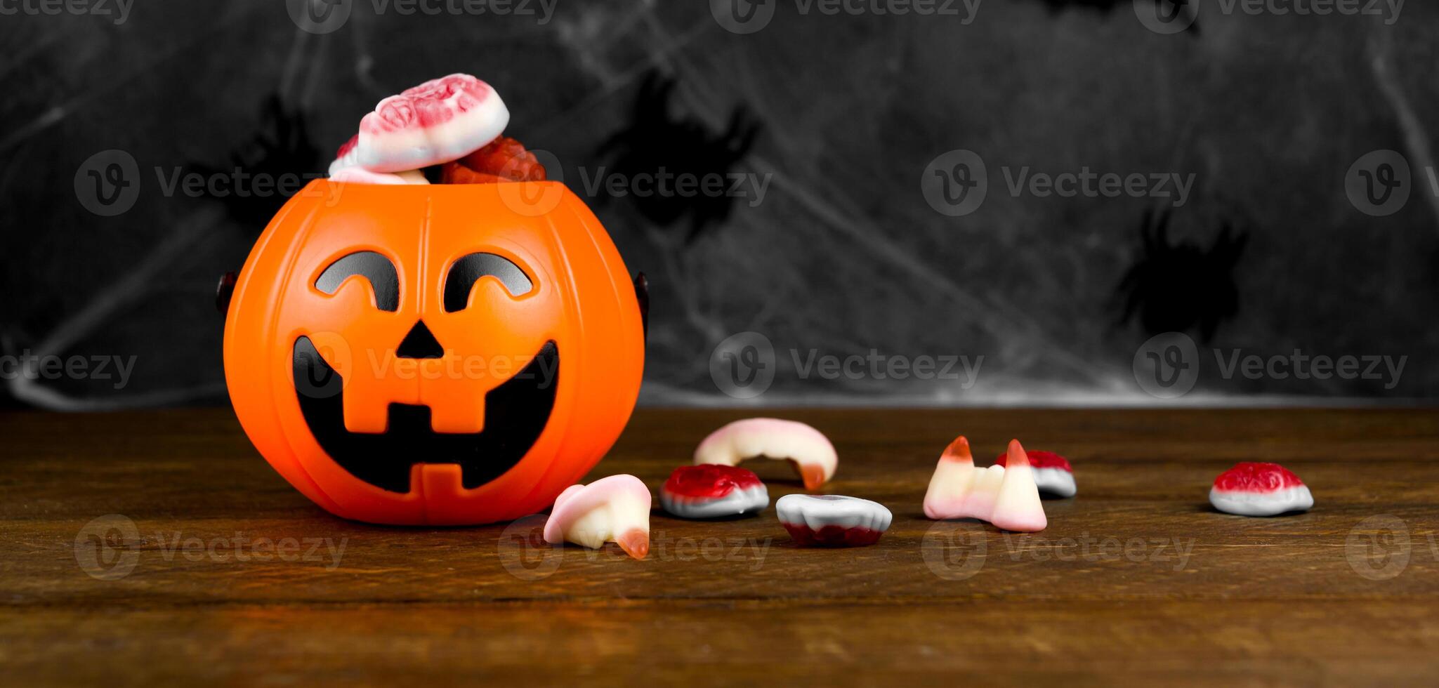 Halloween picture with trick or treat concept.Jack'o'lantern shaped candy bowl with delicios scary sweets on dark background with spiderweb photo