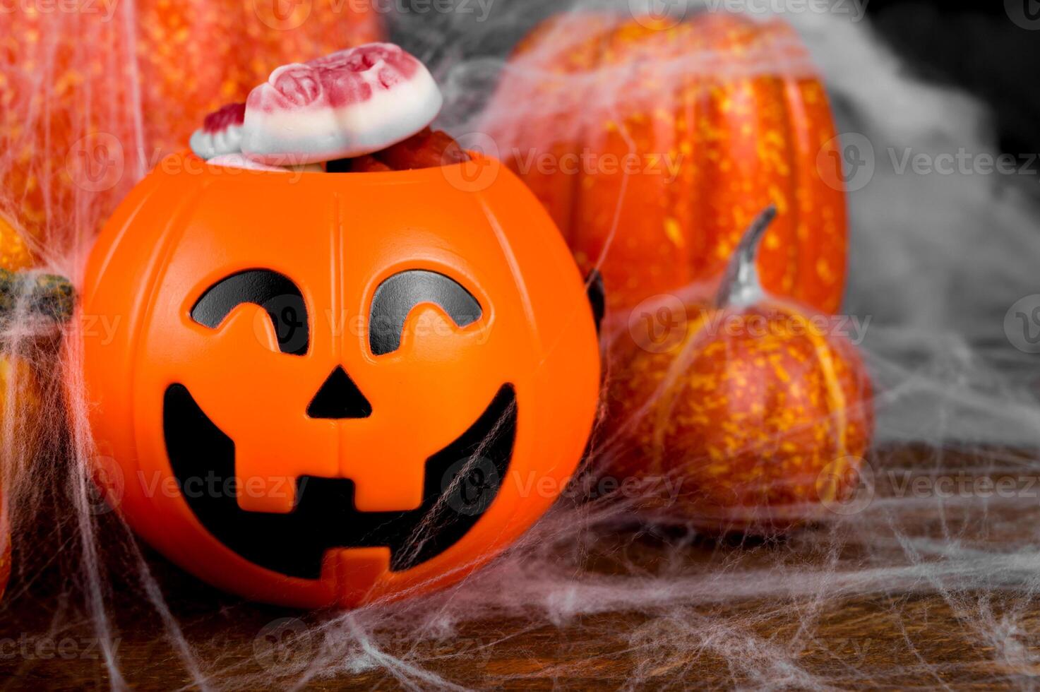 jack-o-lantern candies bowl near pile of pumpkin decorated with spiderweb.Trick or treat concept photo