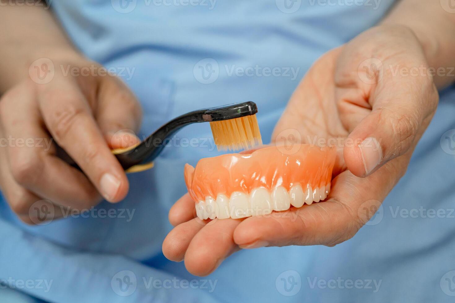 senior woman patient clean teeth denture with toothbrush for chew food. photo
