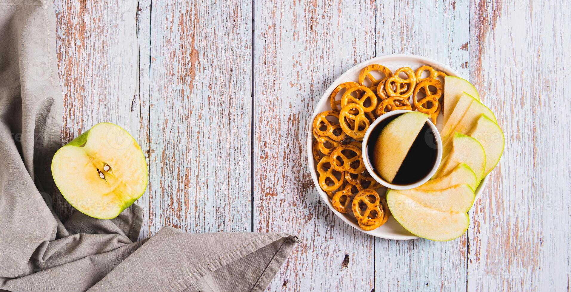 Crispy green apples and pretzels with miso caramel sauce on a plate top view web banner photo