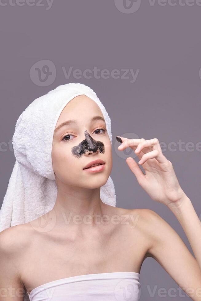 Young caucasian female applying charcoal face mask for blackhead removal and skincare routine. photo