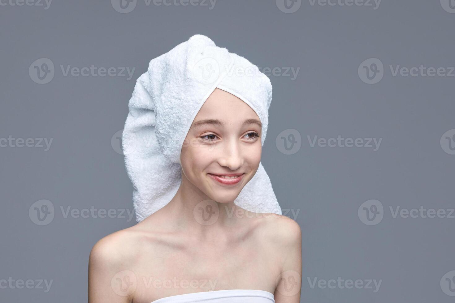 Young caucasian female with towel wrapped hair smiling on gray background. photo