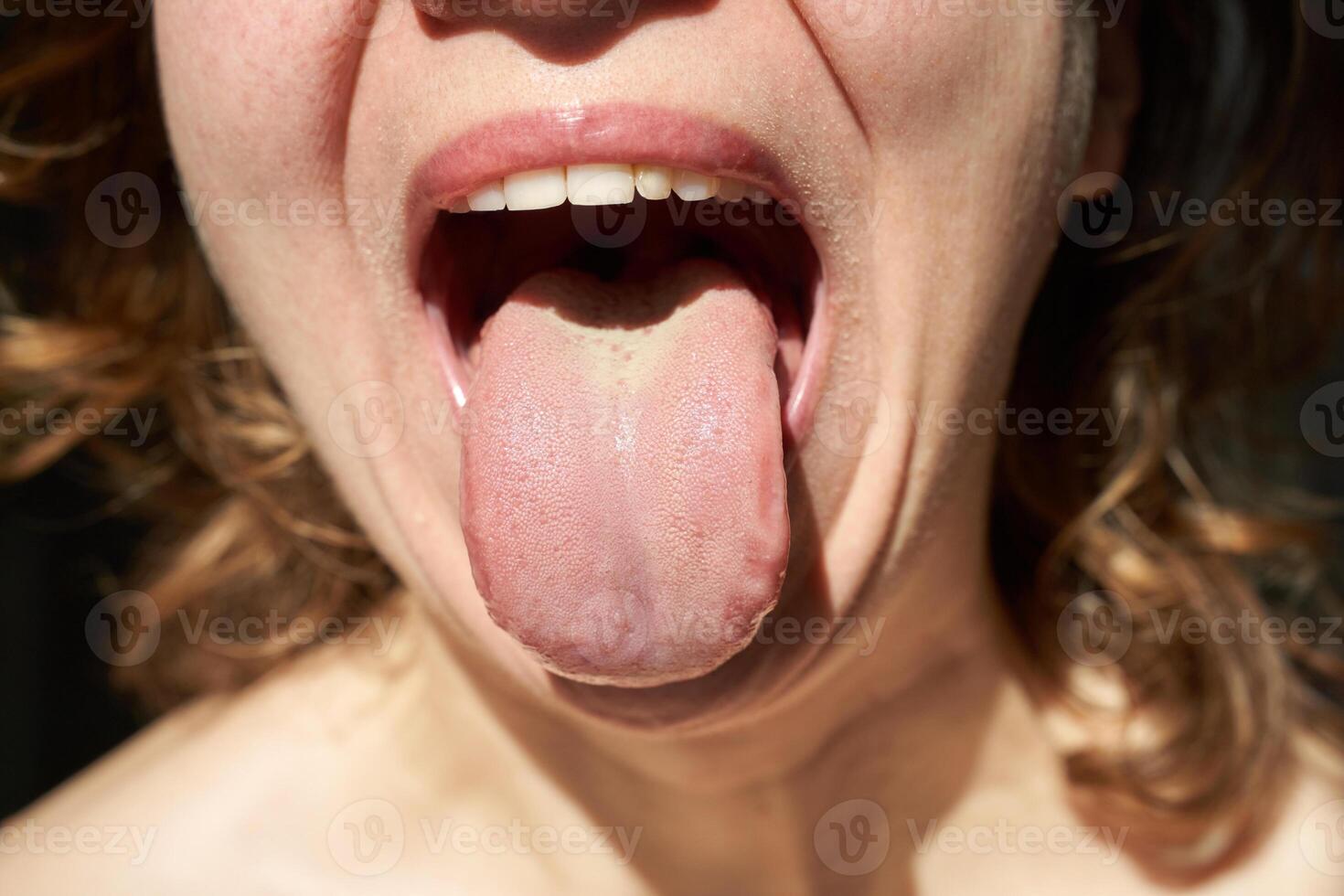 Close-up of caucasian female with open mouth and extended tongue in bright light. photo