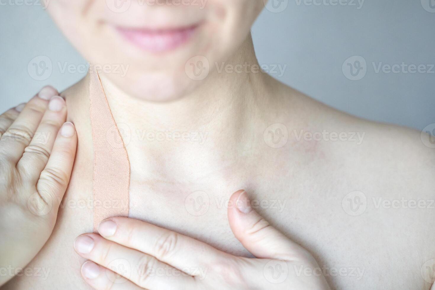 Female adult caucasian applying therapeutic kinesiology tape to shoulder neck area for pain relief. photo