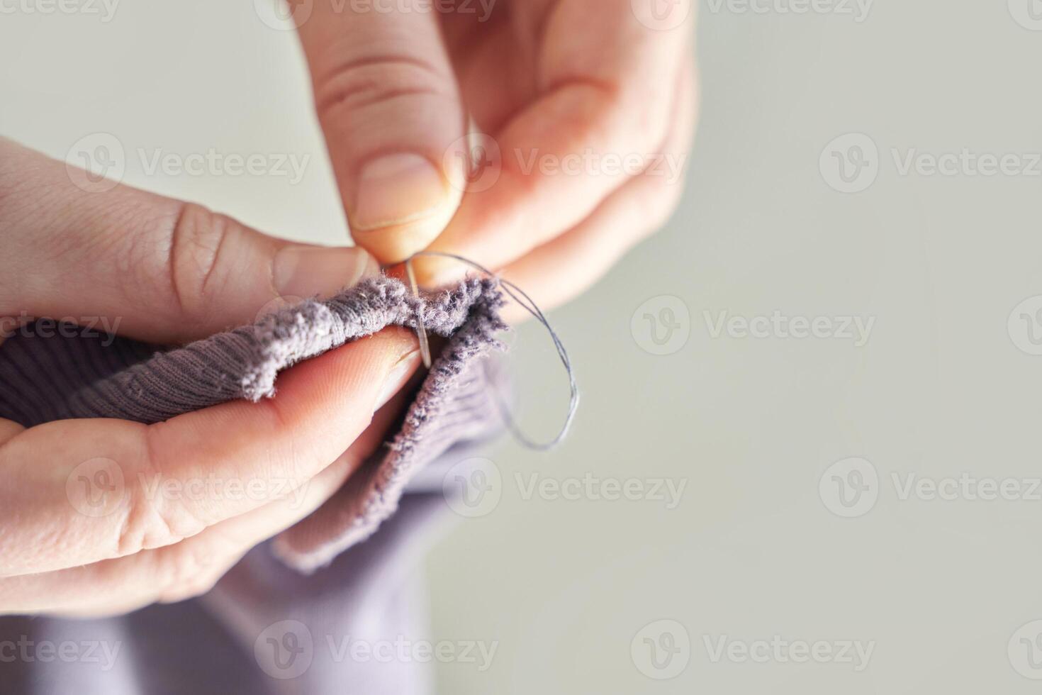 Close-up of hands sewing fabric with needle and thread for repairing and mending, craftsmanship detail. photo