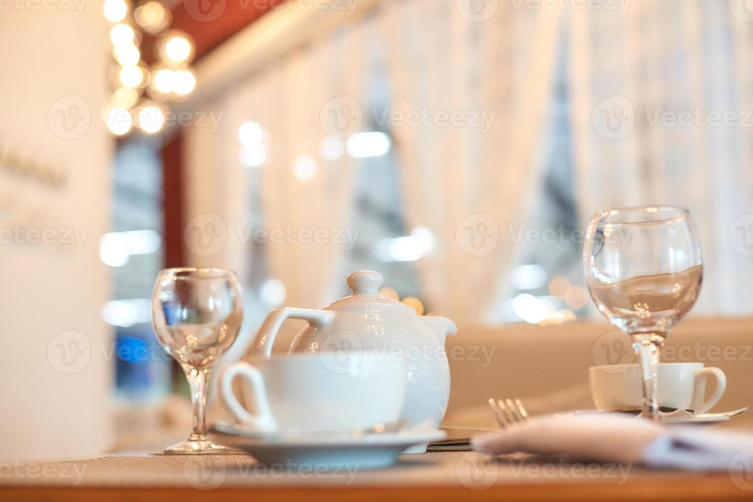 Elegant table setting with white teapot and glassware in cozy cafe ambiance. photo