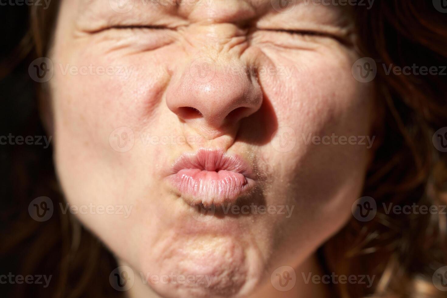 Caucasian female adult making a funny expression with eyes closed and lips puckered. photo