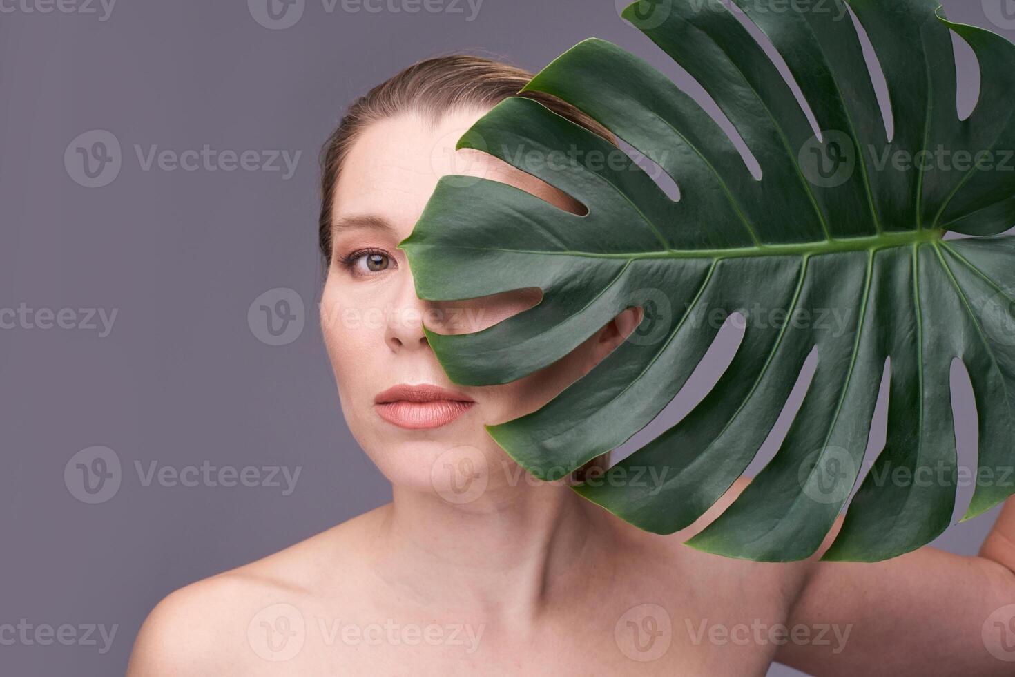 Caucasian adult female with monstera leaf against gray background in artistic minimalist portrait. photo