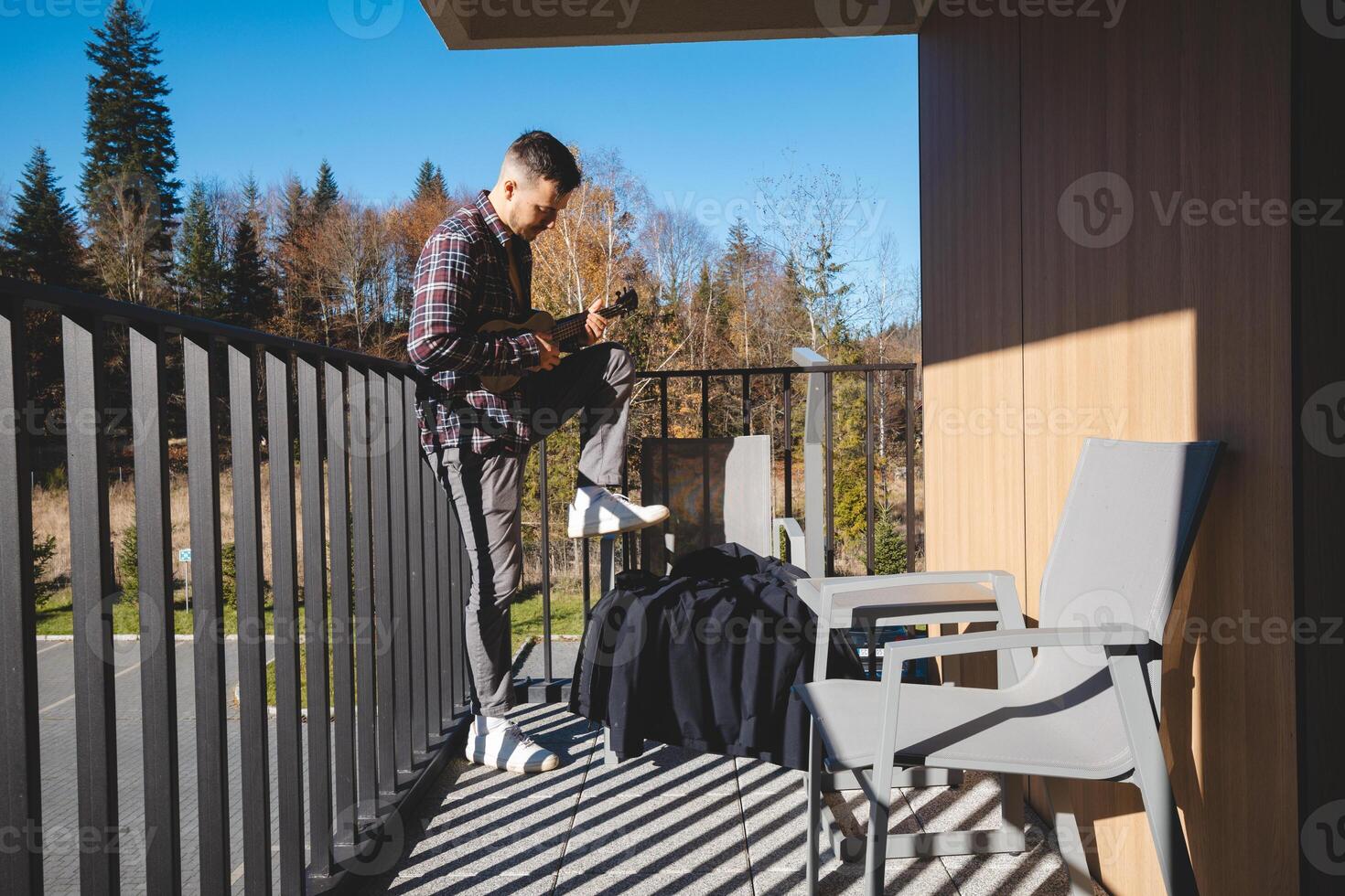 young musician stands on a sunlit balcony. The sound of fall played in soft ukulele tones. photo