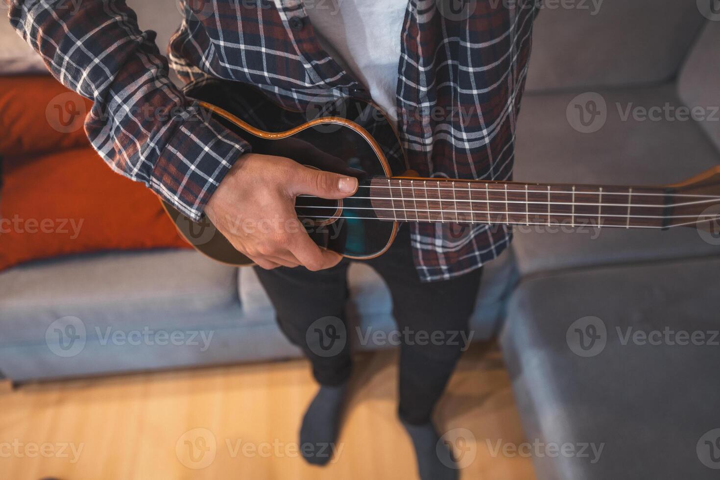 Captures a man's fingers plucking the strings of a glossy black ukulele. Making a music. Pleasure of playing an instrument photo