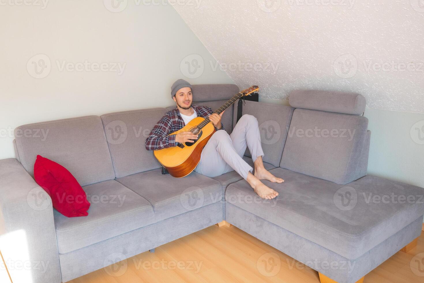 Barefoot hiker lies on a gray couch, strumming an acoustic guitar in a cozy, relaxed atmosphere, lost in the soothing melodies and deep emotional connection to music photo