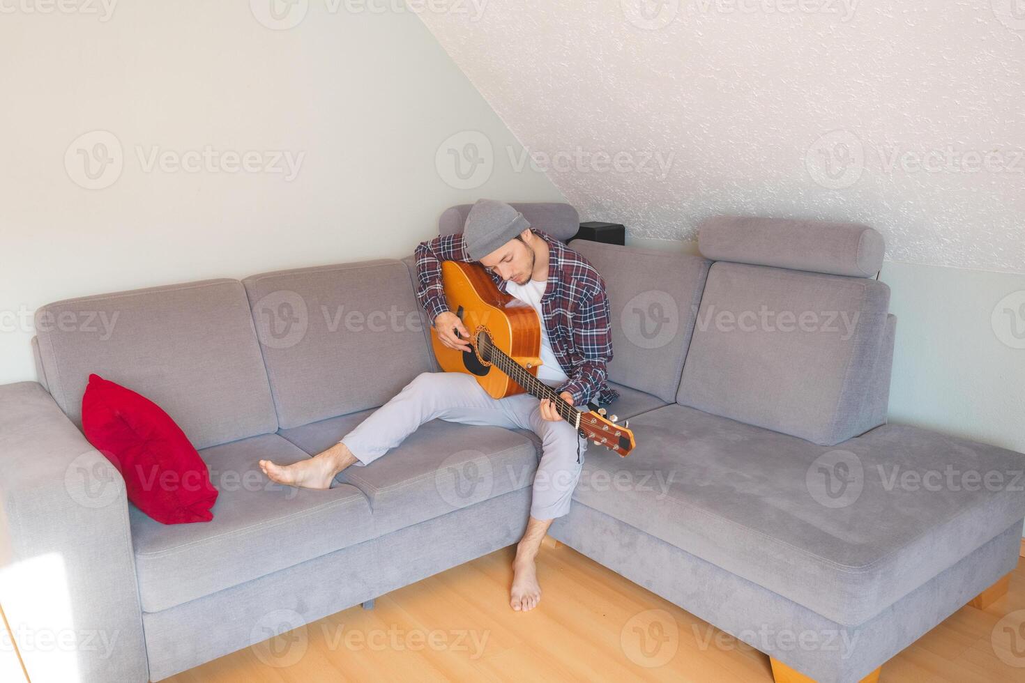 Boy sits comfortably on a gray couch, strumming an acoustic guitar in a cozy, relaxed atmosphere, lost in the soothing melodies and deep emotional connection to music photo