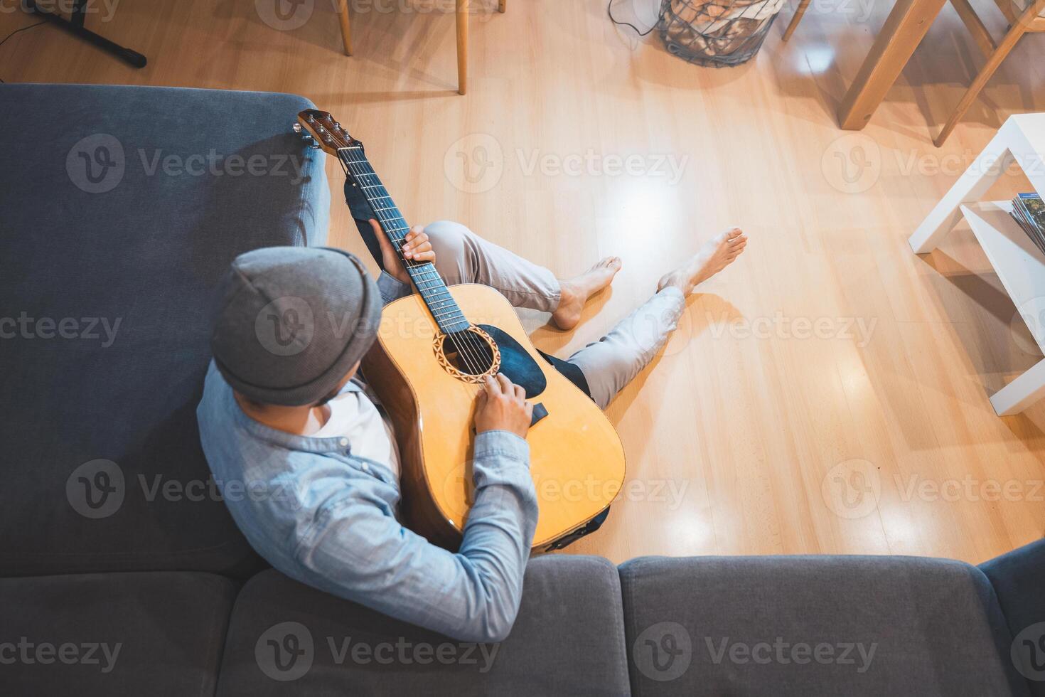 Boy sits on a gray couch, casually strumming an acoustic guitar, immersed in a moment of relaxation and introspection, creating a peaceful and creative atmosphere. Top view photo