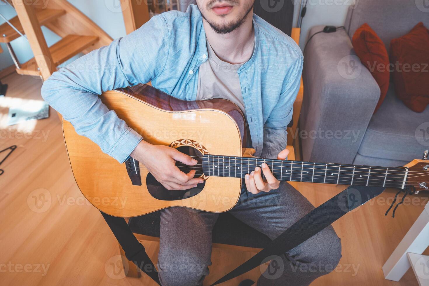 Man focuses while practicing acoustic guitar on a gray sofa photo