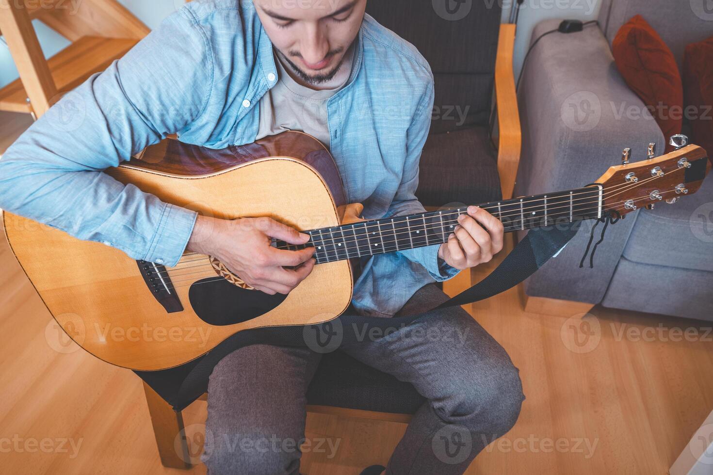 Young man strums an acoustic guitar while sitting on a couch in a relaxed pose photo