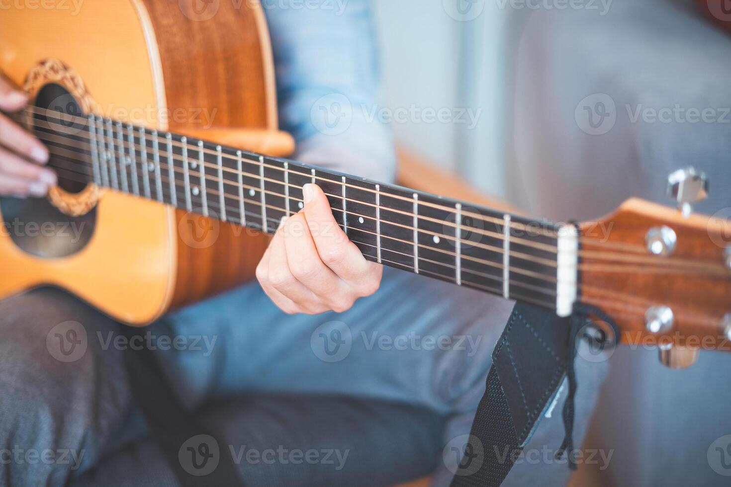 Close-up on male strums an acoustic guitar in a cozy home, immersed in music. His casual style, warm lighting, and relaxed atmosphere create a serene, artistic, and inspiring moment photo