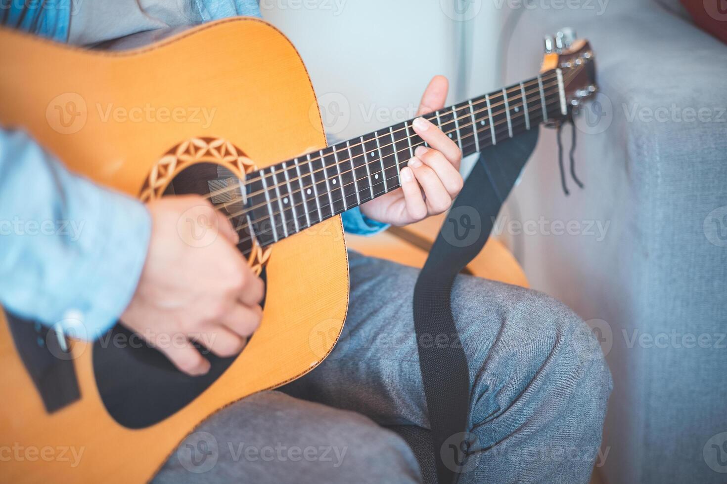Close-up on boy strums an acoustic guitar in a cozy home, immersed in music. His casual style, warm lighting, and relaxed atmosphere create a serene, artistic, and inspiring moment photo