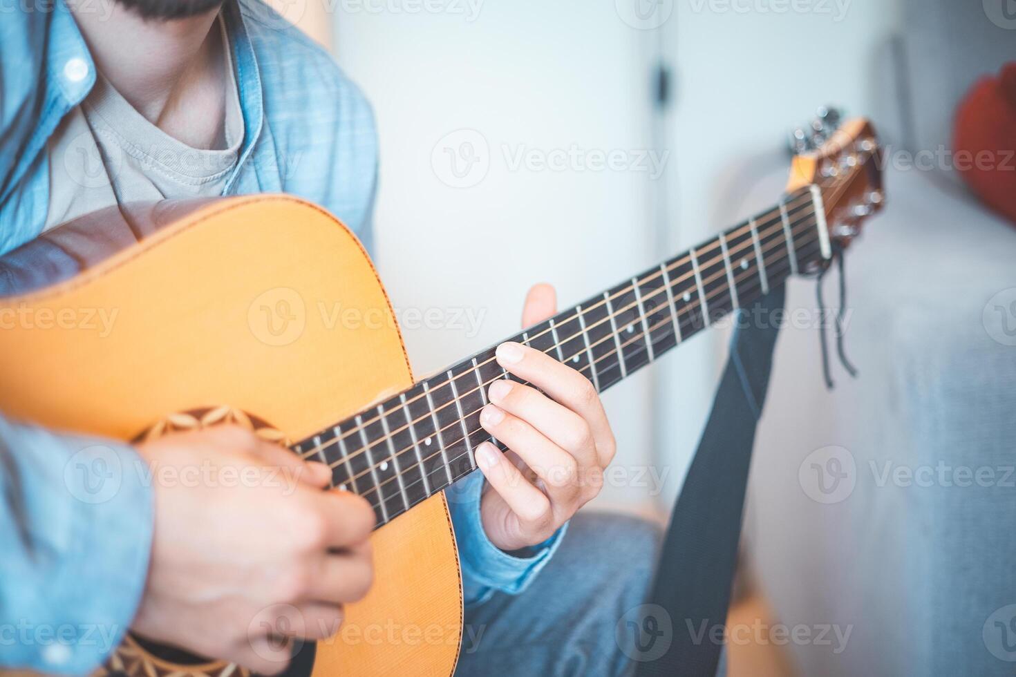 Close-up on man strums an acoustic guitar in a cozy home, immersed in music. His casual style, warm lighting, and relaxed atmosphere create a serene, artistic, and inspiring moment photo