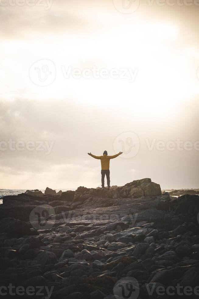 Curious man walks along a rocky beach during a breathtaking stormy sunset in western Iceland, enjoying the last rays of sunlight. Dramatic sky and soft Arctic light photo