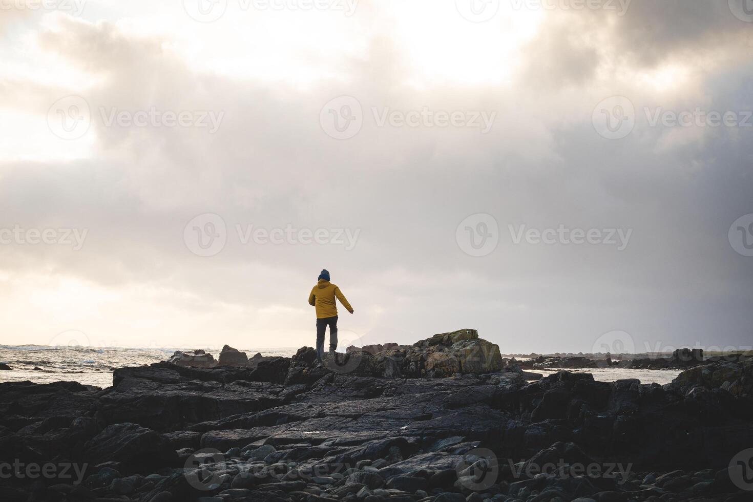 Happy traveler walks along a rocky beach during a breathtaking stormy sunset in western Iceland, enjoying the last rays of sunlight. Dramatic sky and soft Arctic light photo