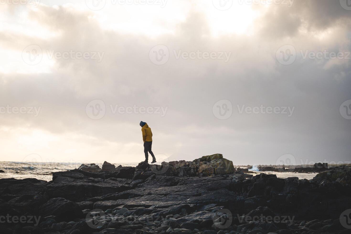 Boy walks along a rocky beach during a breathtaking stormy sunset in western Iceland, enjoying the last rays of sunlight. Dramatic sky and soft Arctic light photo