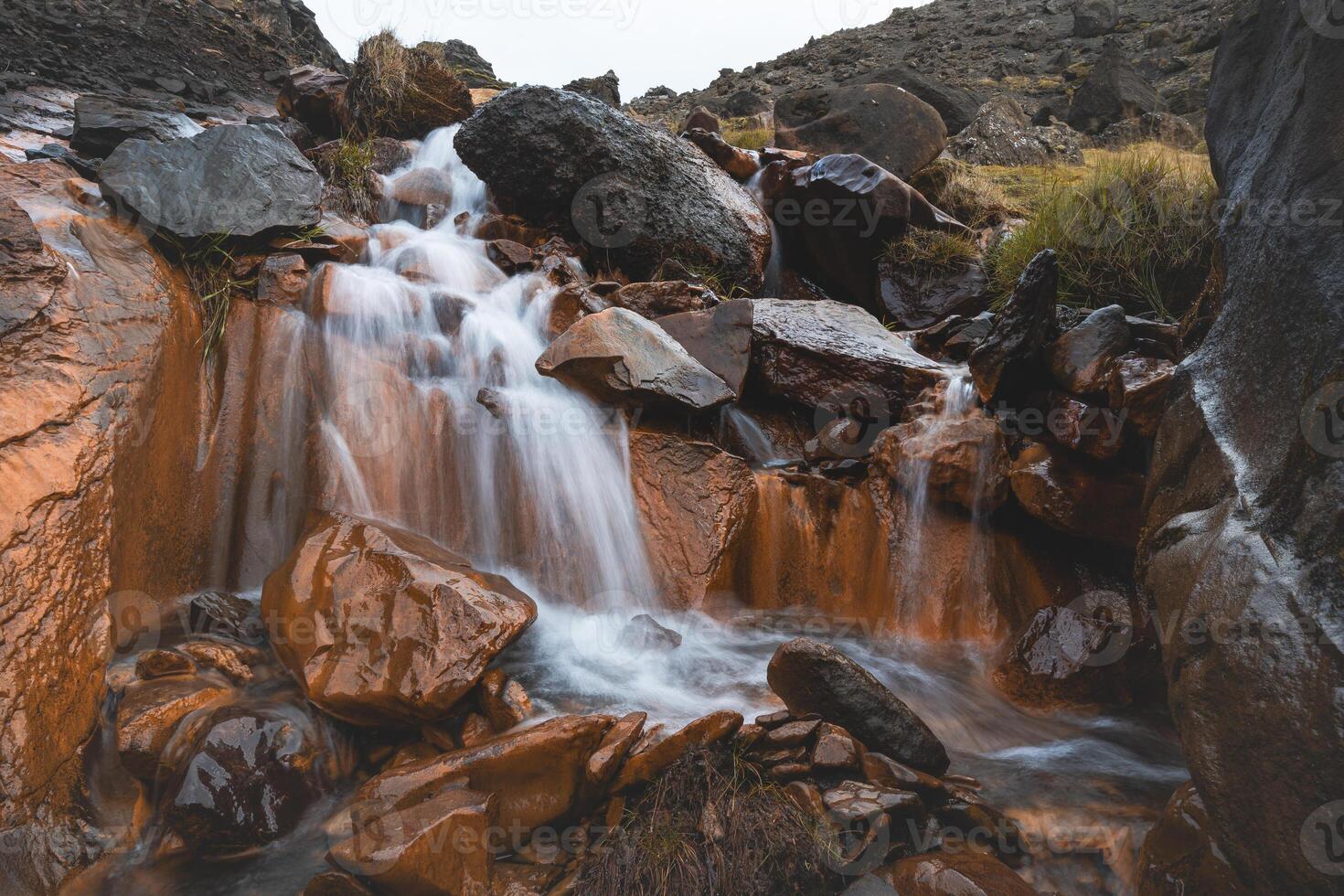 Rust colored waterfall flows through volcanic rocks in Iceland wild highlands, where fire meets water in a surreal, untouched symphony photo