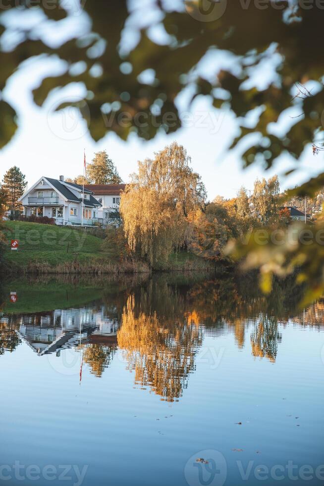 reflections dance on the still waters of Holmendammen Lake in Oslo, surrounded by colorful trees and hillside homes under a crisp, cloudless sky photo