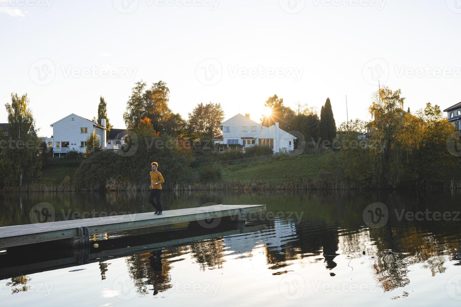 Lone man walks on pier an Oslo lake, Holmendammen as the sun sets behind charming houses, capturing a peaceful moment of reflection and stillness in Norway autumn magic photo