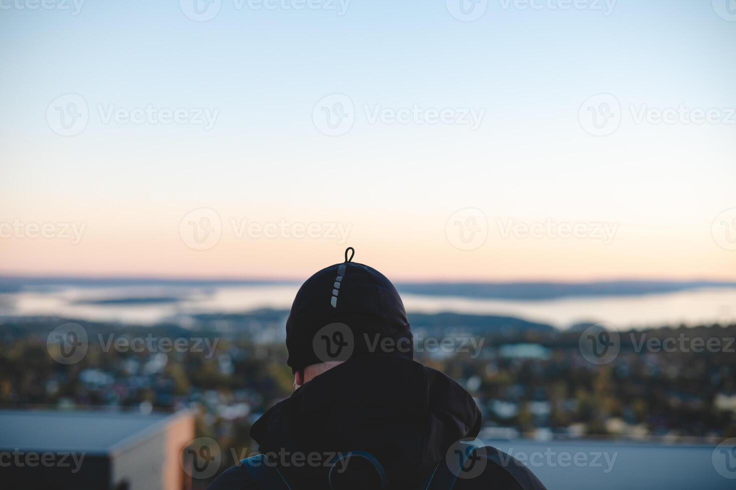 Overlooking Oslo from above, a traveler watches the sunset paint the horizon in peach and blue, embracing a serene Scandinavian evening from the heights photo