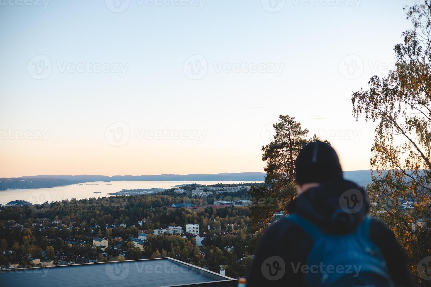 Oslo from above, a traveler watches the sunset paint the horizon in peach and blue, embracing a serene Scandinavian evening from the heights photo
