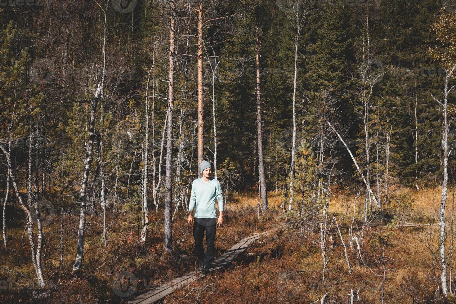 Adventurer walks on a narrow wooden trail in Oslo Marka, surrounded by golden autumn light and the silent whisper of Nordic wilderness photo