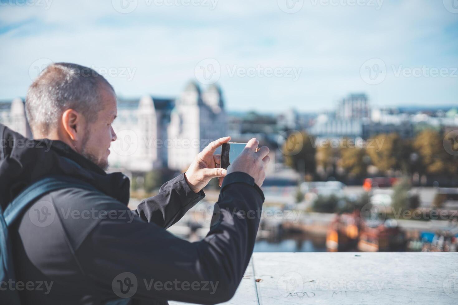 Capturing Oslo from Opera house, a traveler frames the city through his phone. Old man is using modern technology photo
