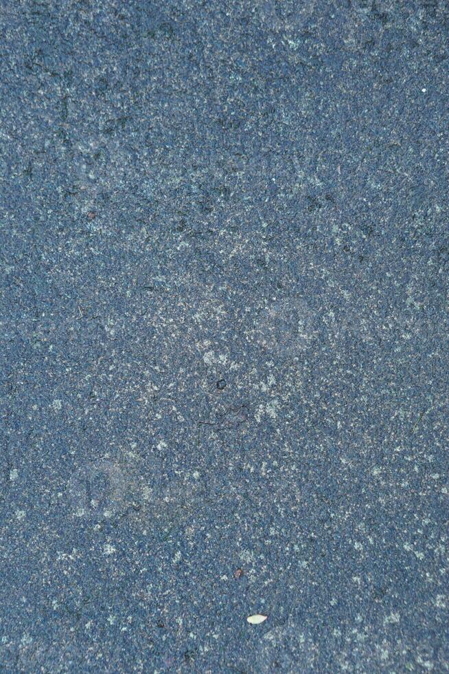 Dark speckled asphalt texture with a small leaf fragment, creating a unique surface pattern photo