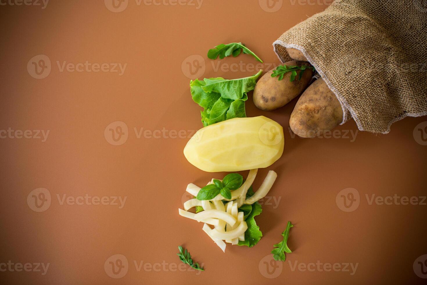 Root vegetable in a sack and sliced potatoes on a brown background photo