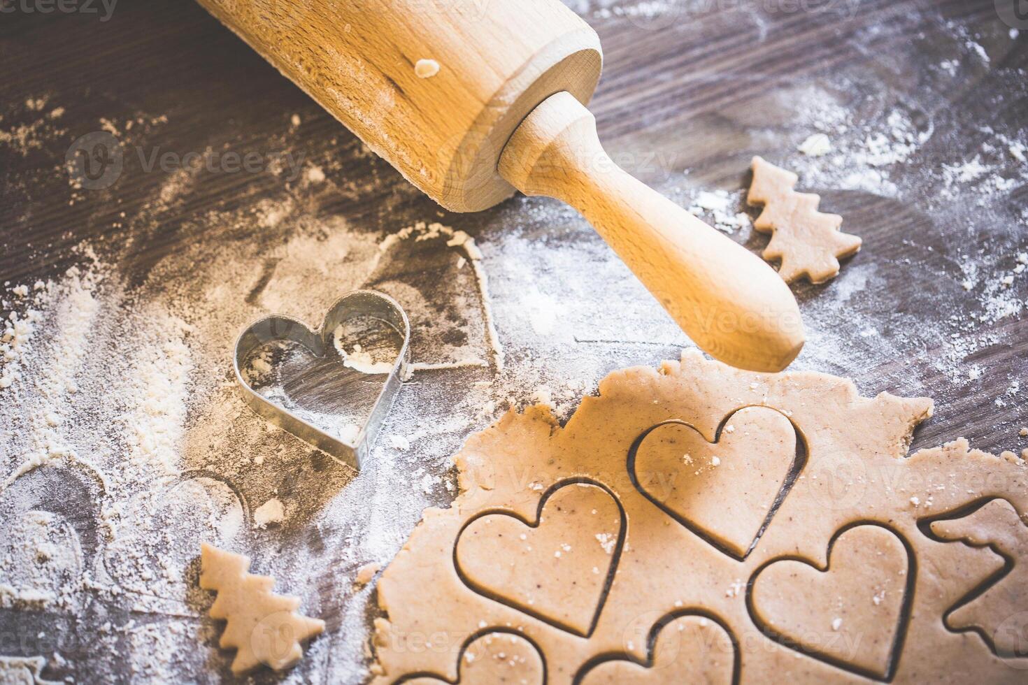 Close up of cookie dough with heart shapes and a rolling pin on a floured surface ready for baking photo