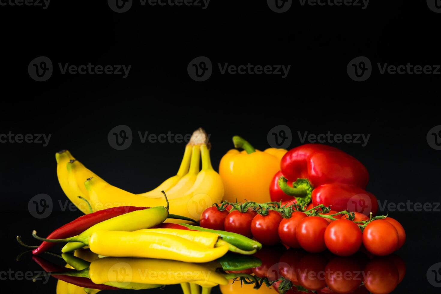 Still life of bananas peppers and tomatoes against a black background with reflections visible photo