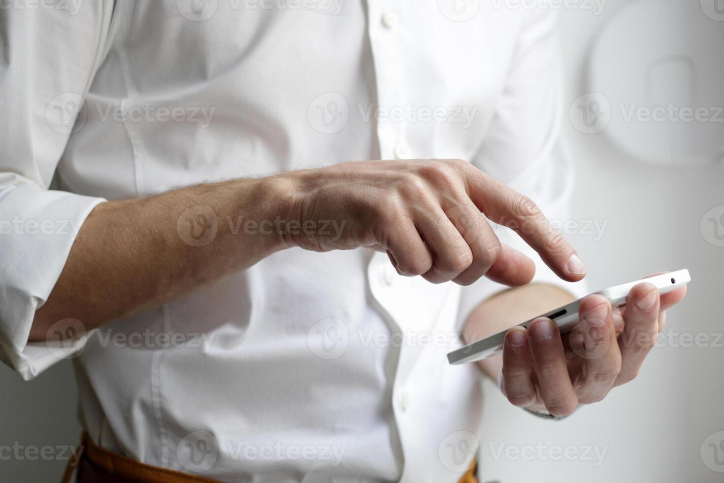 Man in white shirt uses smartphone with hands visible against a plain light background indoors scene photo