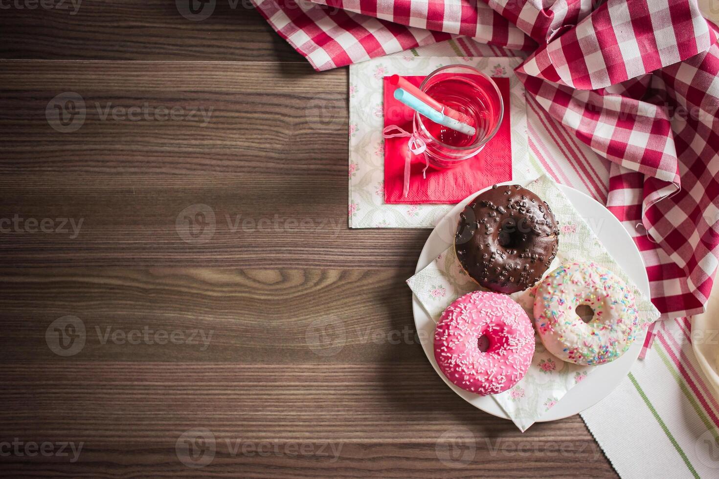 Overhead view of donuts and a drink on a wooden table with checkered and striped cloths around it photo