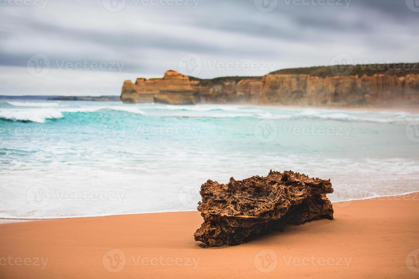A rock formation on a sandy beach with ocean waves and cliffs in the distant background view scene photo