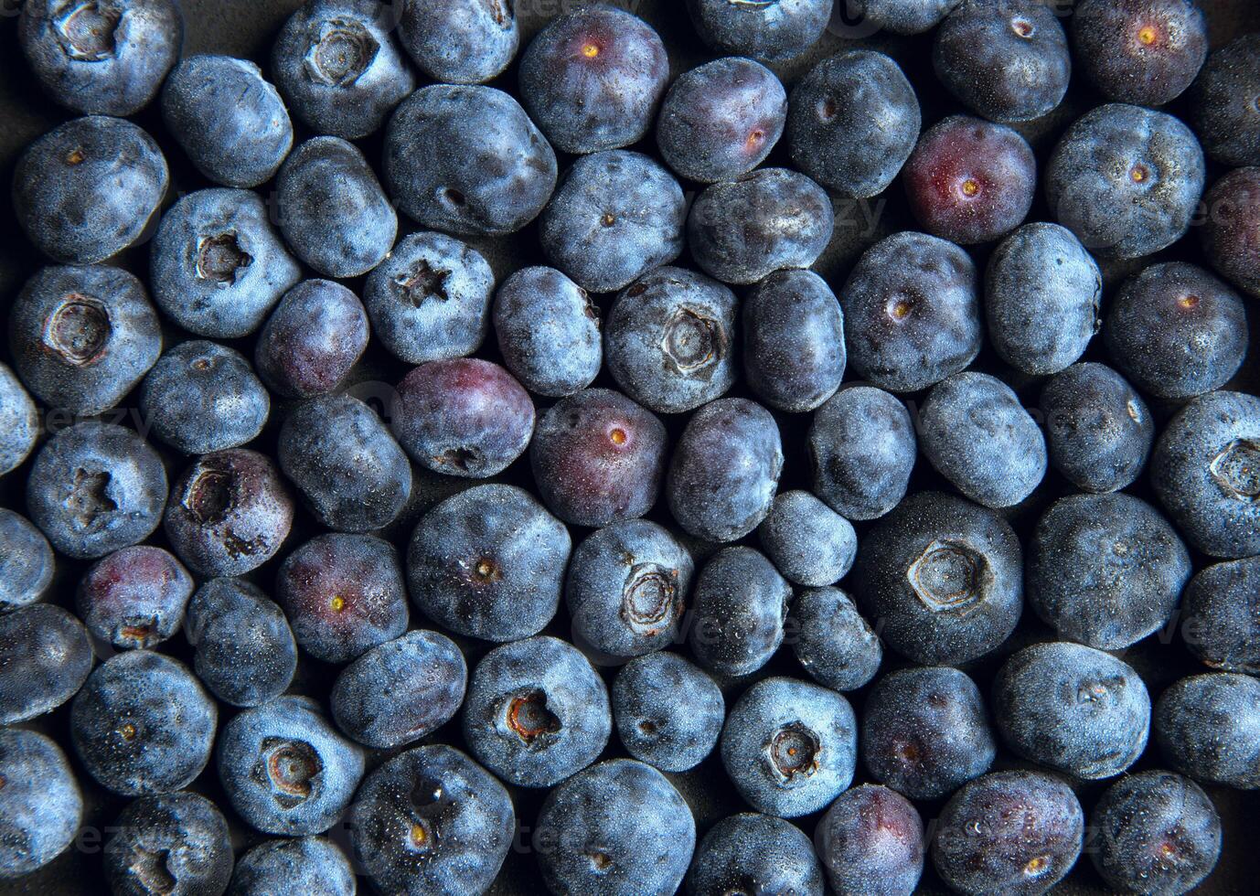 A close up of a pile of fresh blueberries showing their texture and color variations on a flat surface photo