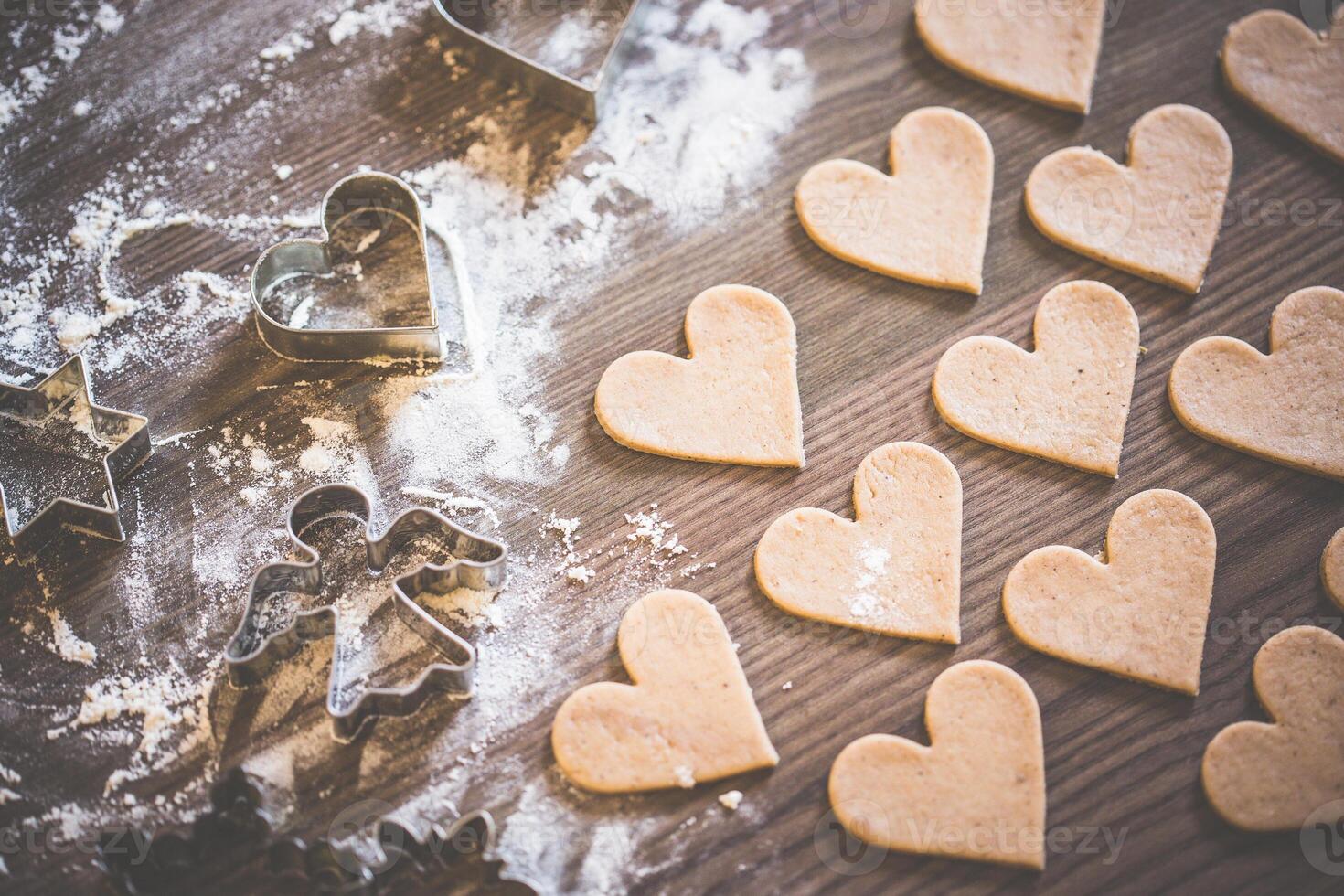 Heart shaped cookies and cookie cutters on a floured wooden surface ready for baking treats photo