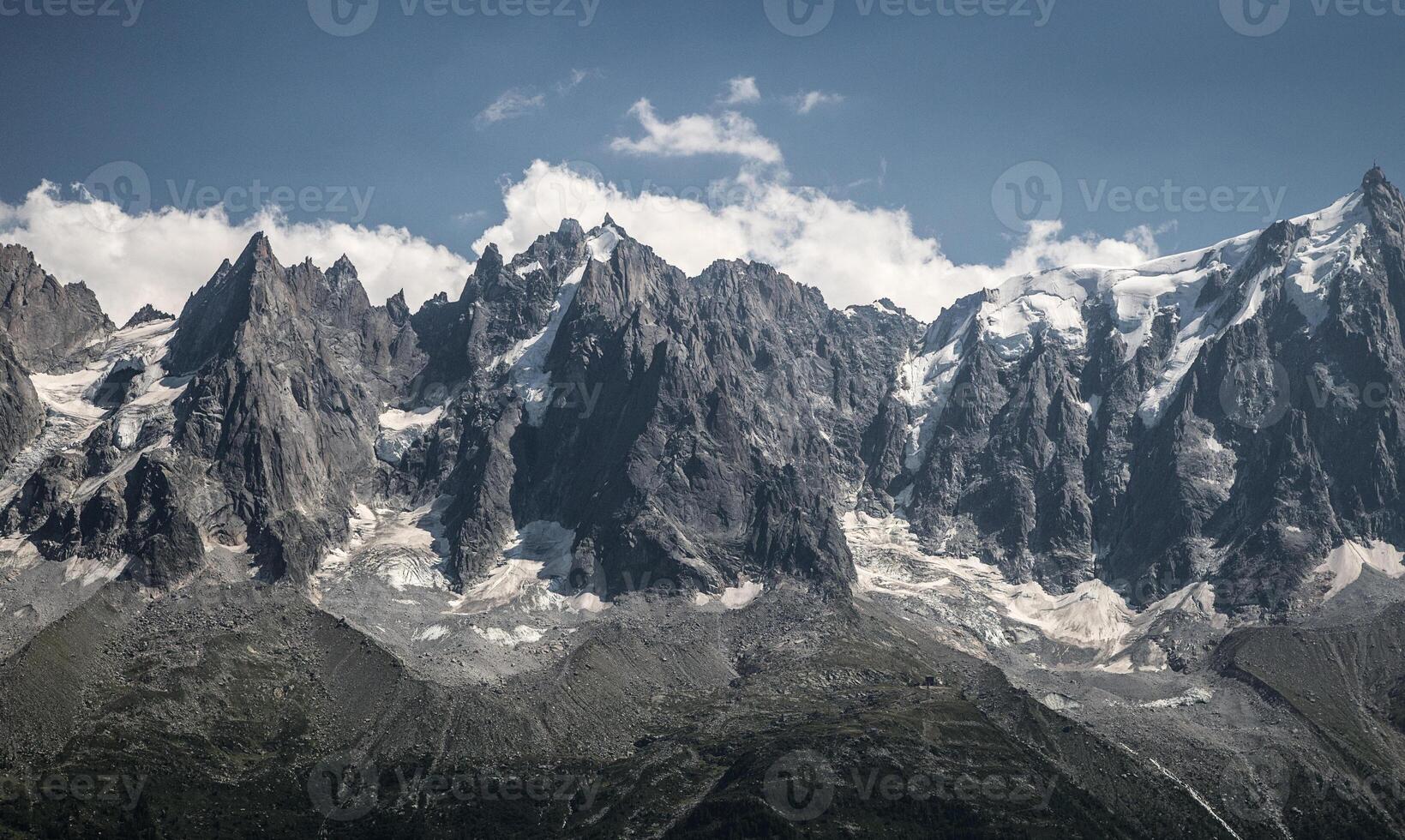 A view of jagged mountain peaks with snow and glaciers under a partly cloudy sky on a sunny day photo