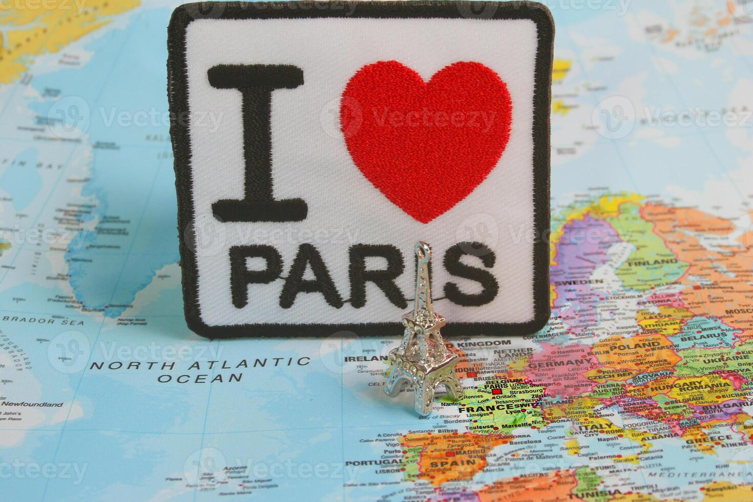 Handcrafted embroidery reading I LOVE PARIS with a red heart, paired with a small silver Eiffel Tower model. Displayed on a world map, centered on France. Perfect for travel and Paris-themed concepts. photo