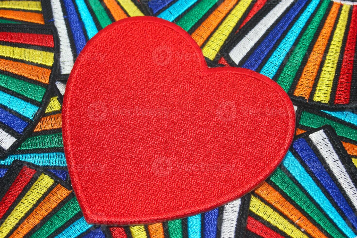 Handmade embroidery of a large red heart crafted from thread and fabric resting on a vibrant rainbow-colored textile background. Perfect for Valentine Day weddings and romantic celebrations photo