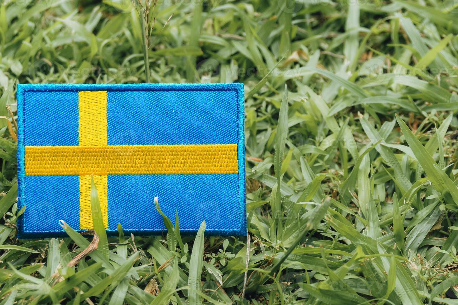 Eco-style Swedish flag made of fabric and thread, leaning on green grass, placed left with text space on right. Environmental, Earth Day, nature-friendly theme. photo