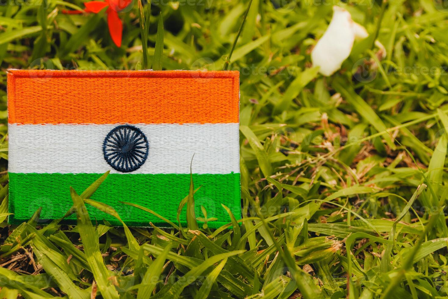 Eco friendly India flag, hand embroidered with natural fabric, placed on green grass with soft white and red flower petals. Left composition with copy space for Middle East Green Initiative themes. photo
