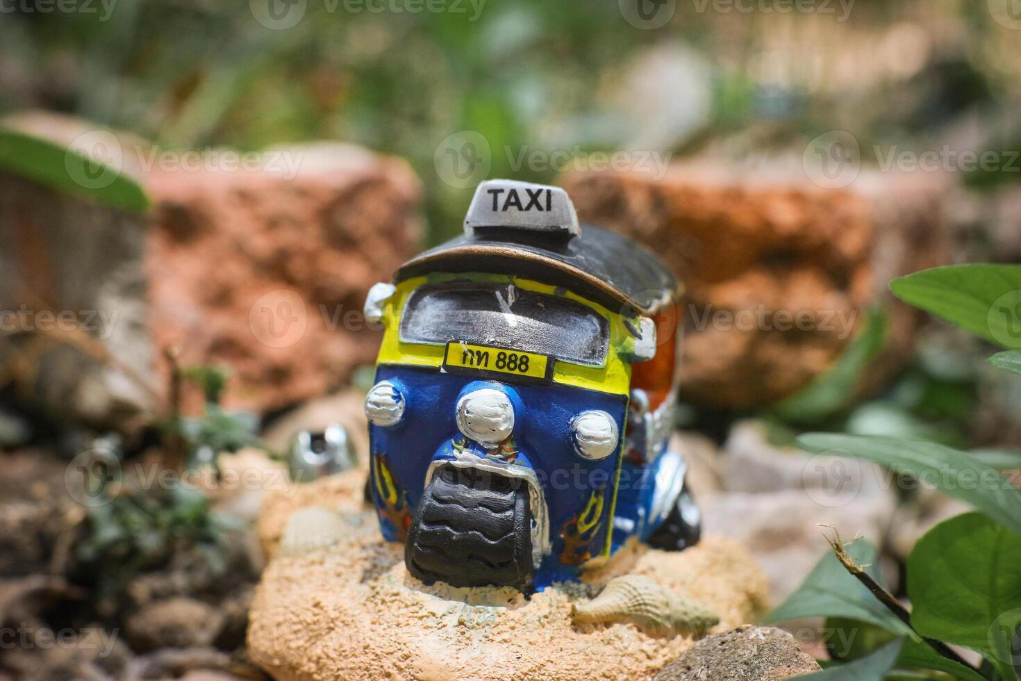 Close-up of colorful miniature Thai tuk-tuk sculpture placed centrally with a rustic, soft-focus background of brown stone, evoking ancient countryside vibes. Natural light, cultural charm. photo