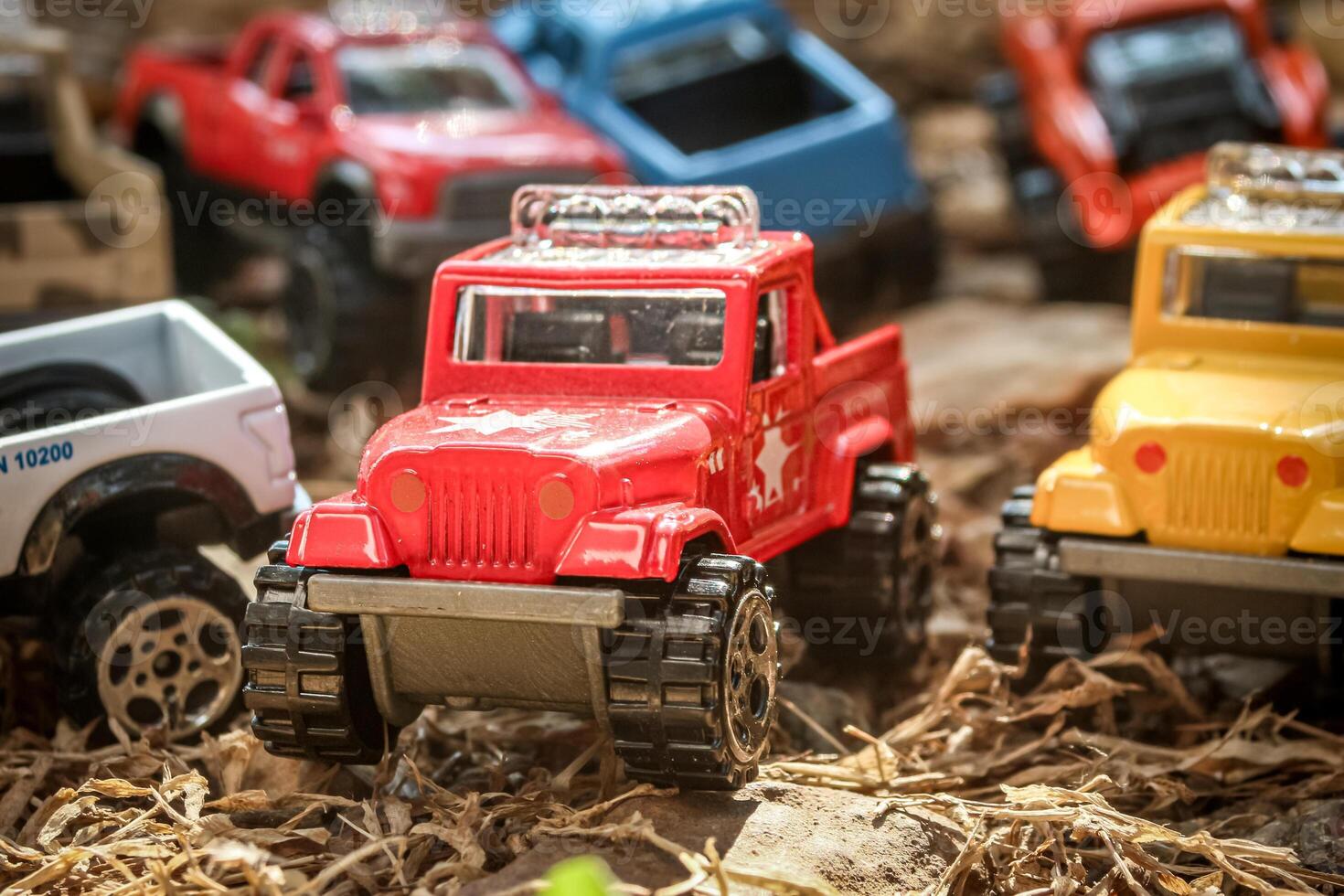 Creative miniature scene of seven colorful 4x4 pickup trucks parked on dry rural grass, simulating an off-road gathering. Front view with four trucks in soft-focus background for depth effect. photo